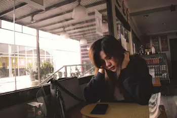 Mujer pensativa en una cafetería apoyada sobre sus manos, evocando la soledad y la rutina