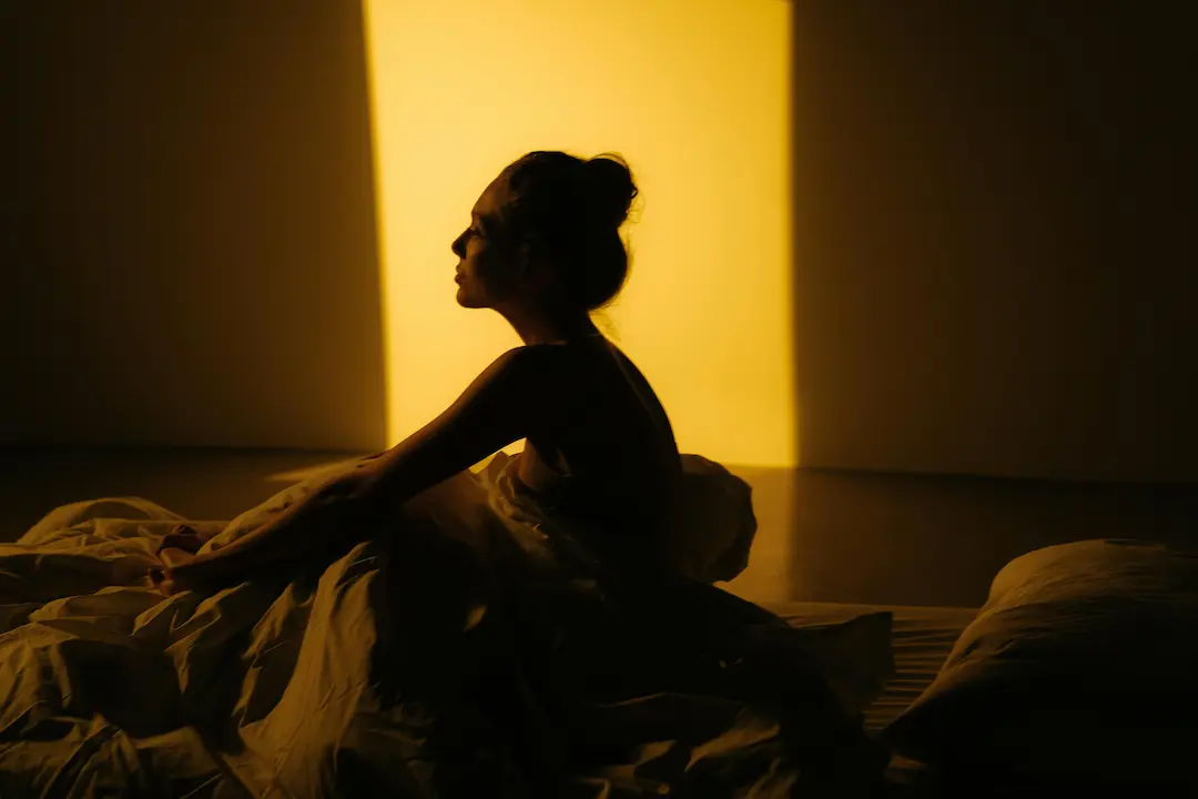 Silueta de una mujer sentada en la cama bajo una luz cálida, simbolizando el descubrimiento del placer femenino y la intimidad consciente