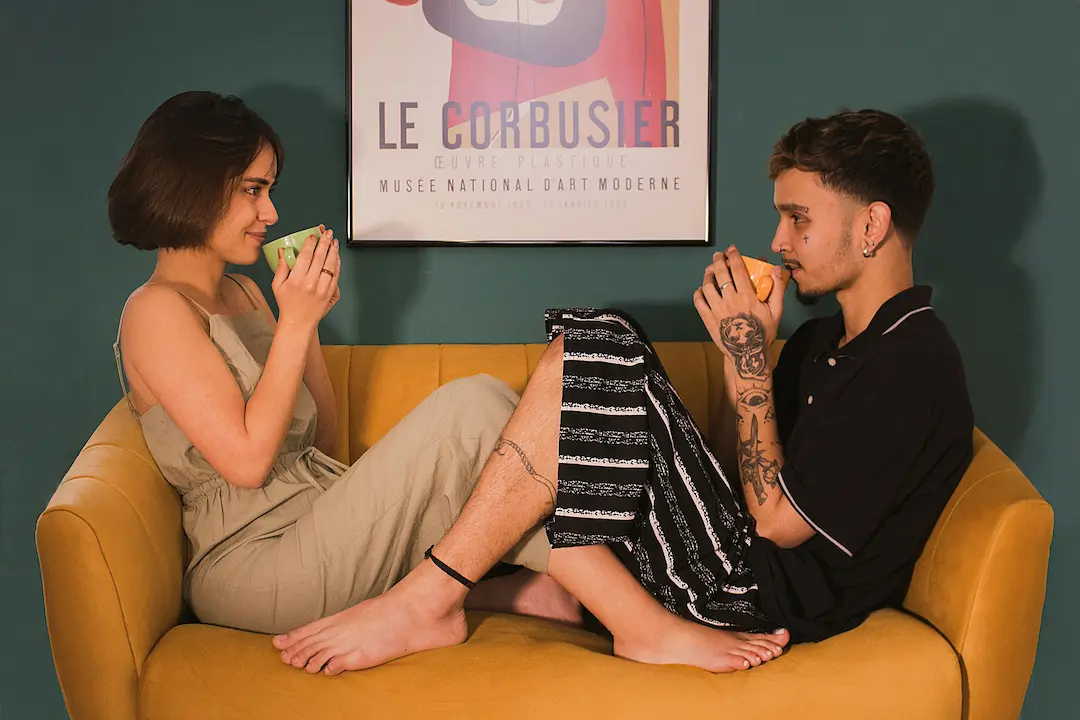 Pareja joven sentada en un sofá compartiendo un café y mirándose con complicidad, representando el cultivo del deseo intencional.