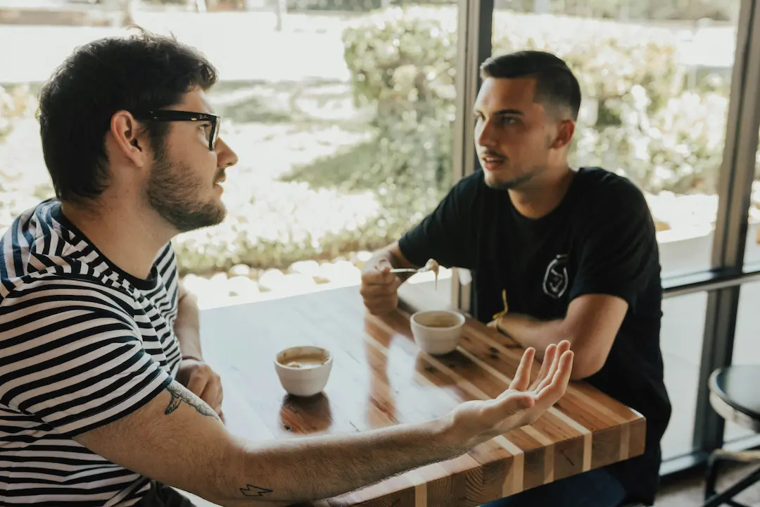 Dos hombres conversando de forma cercana en una mesa con café, representando la comunicación abierta y el intercambio de ideas en la relación.